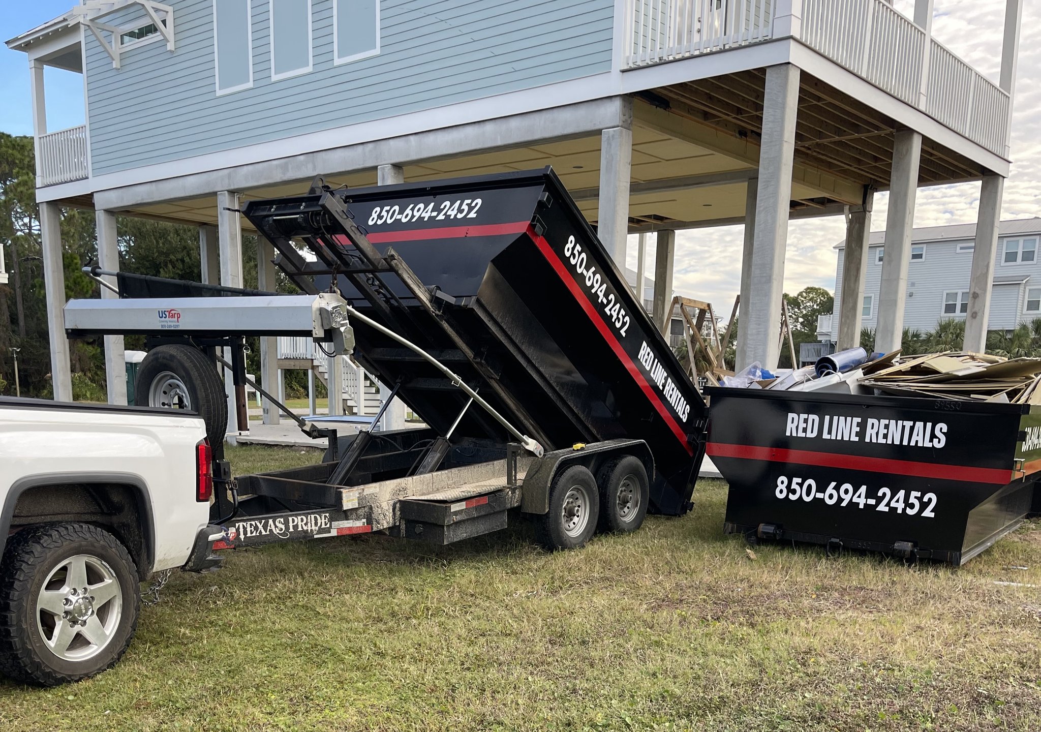 Black Red Line Roll-Offs truck loading a roll-off dumpster on a wooded lot in Crawfordville, FL